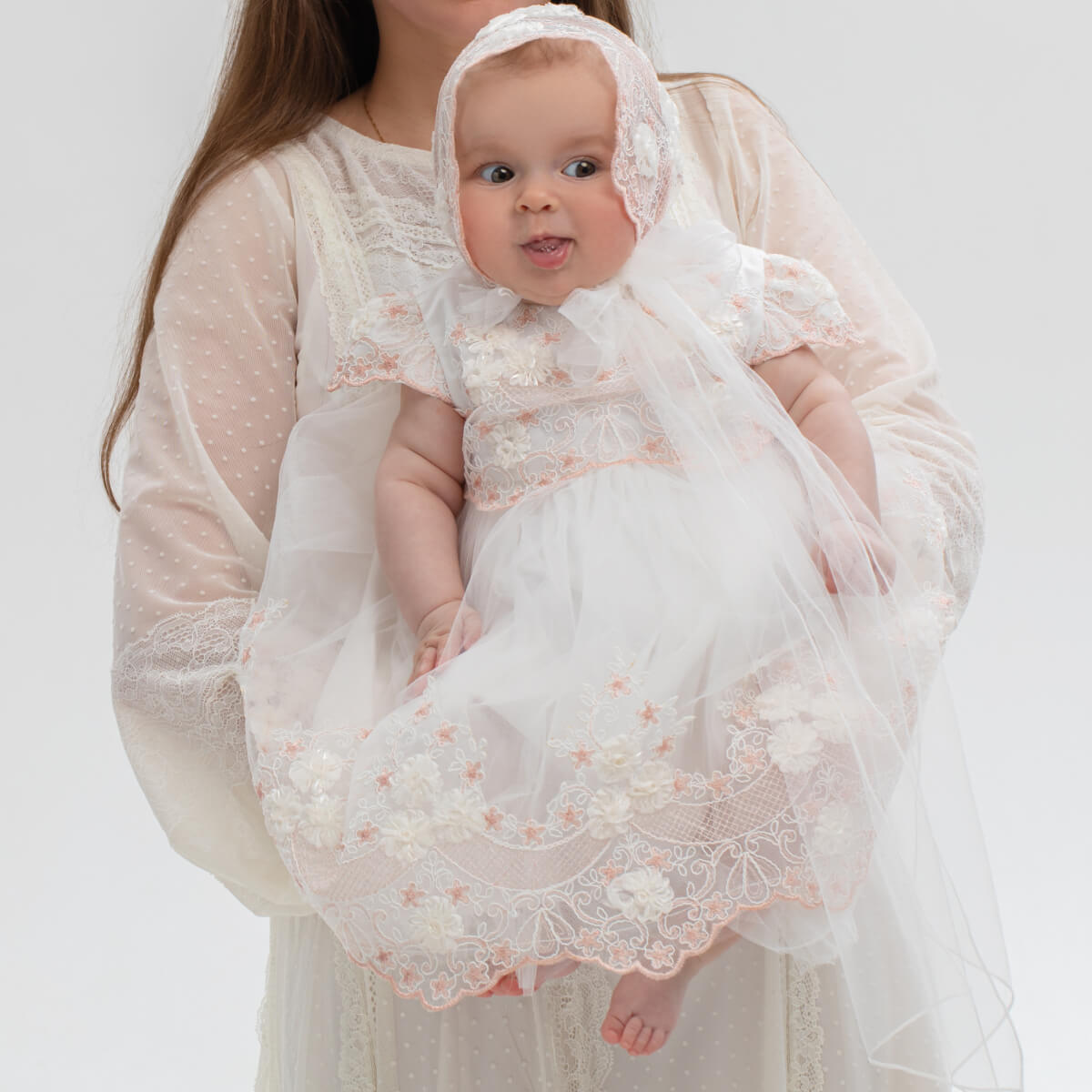 Baby in a Baptism Dress with Floral Lace held by a person against a plain background