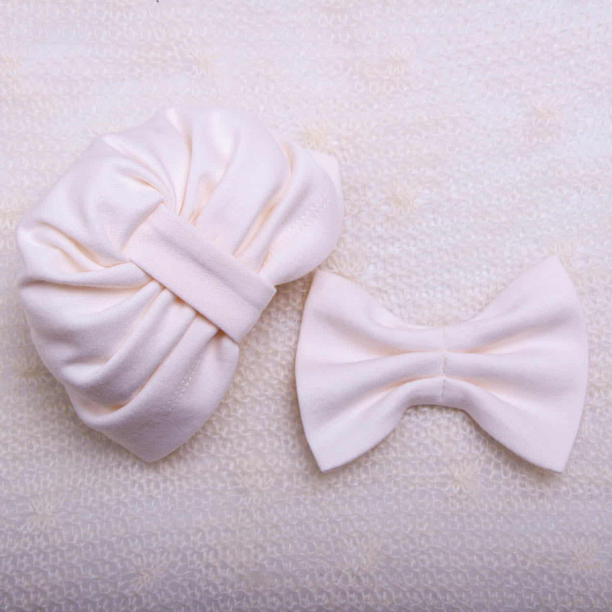 Two white hair accessories, a bow and a headband, on a textured beige background.