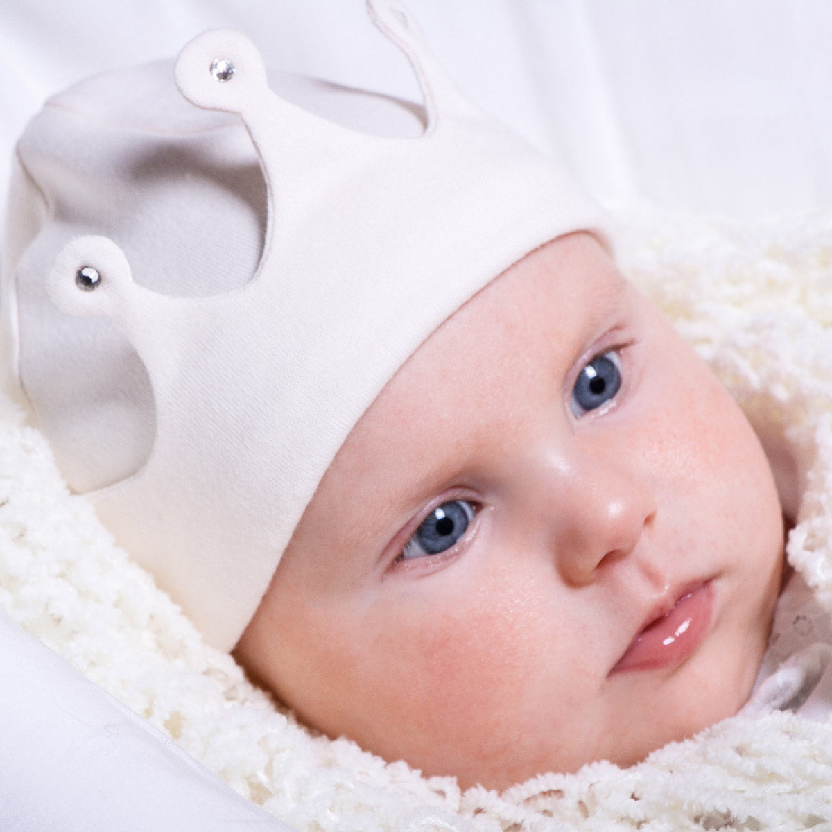 Close-up of a baby wearing a white hat with a decorative element on a light background