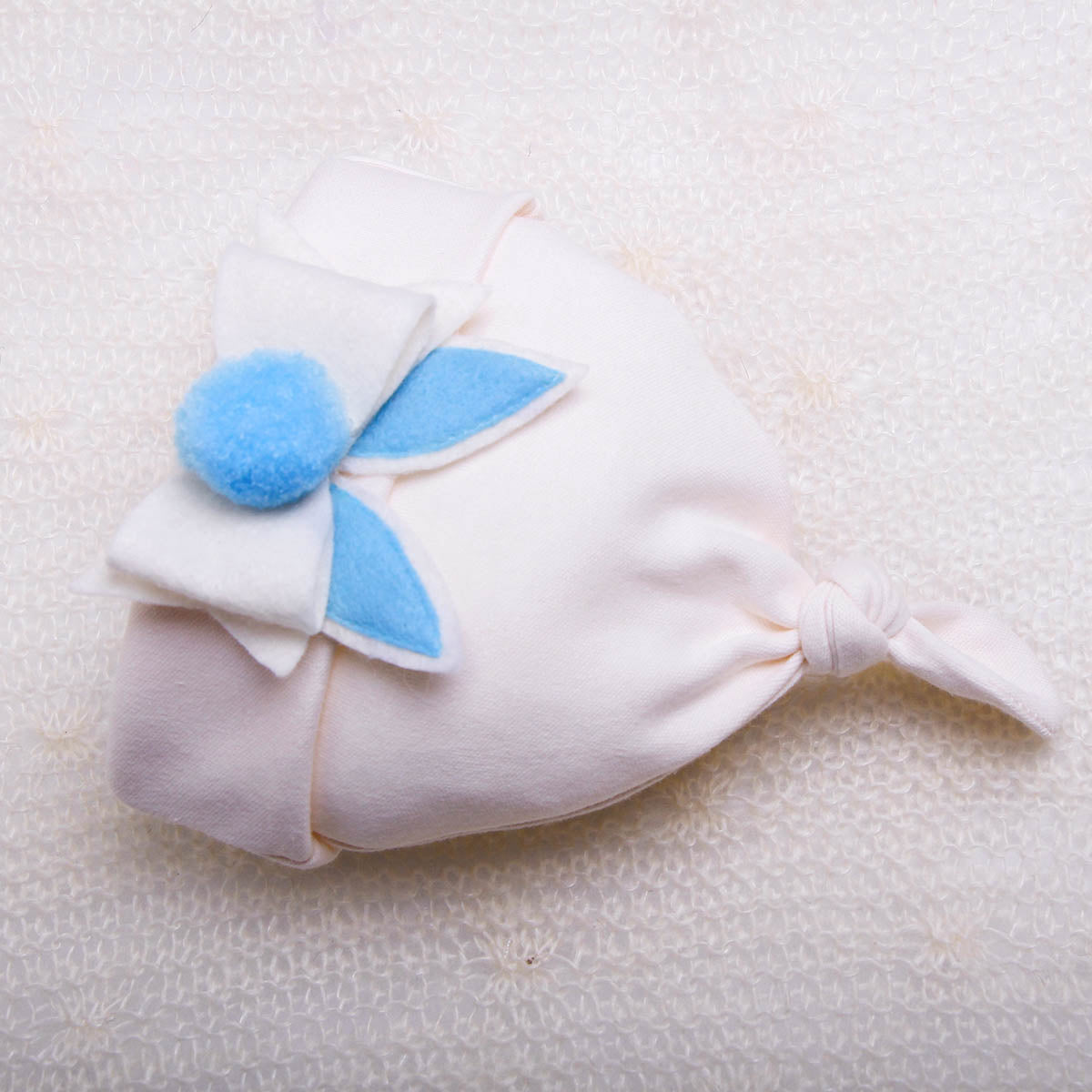 White baby hat with blue flower details on a textured white background