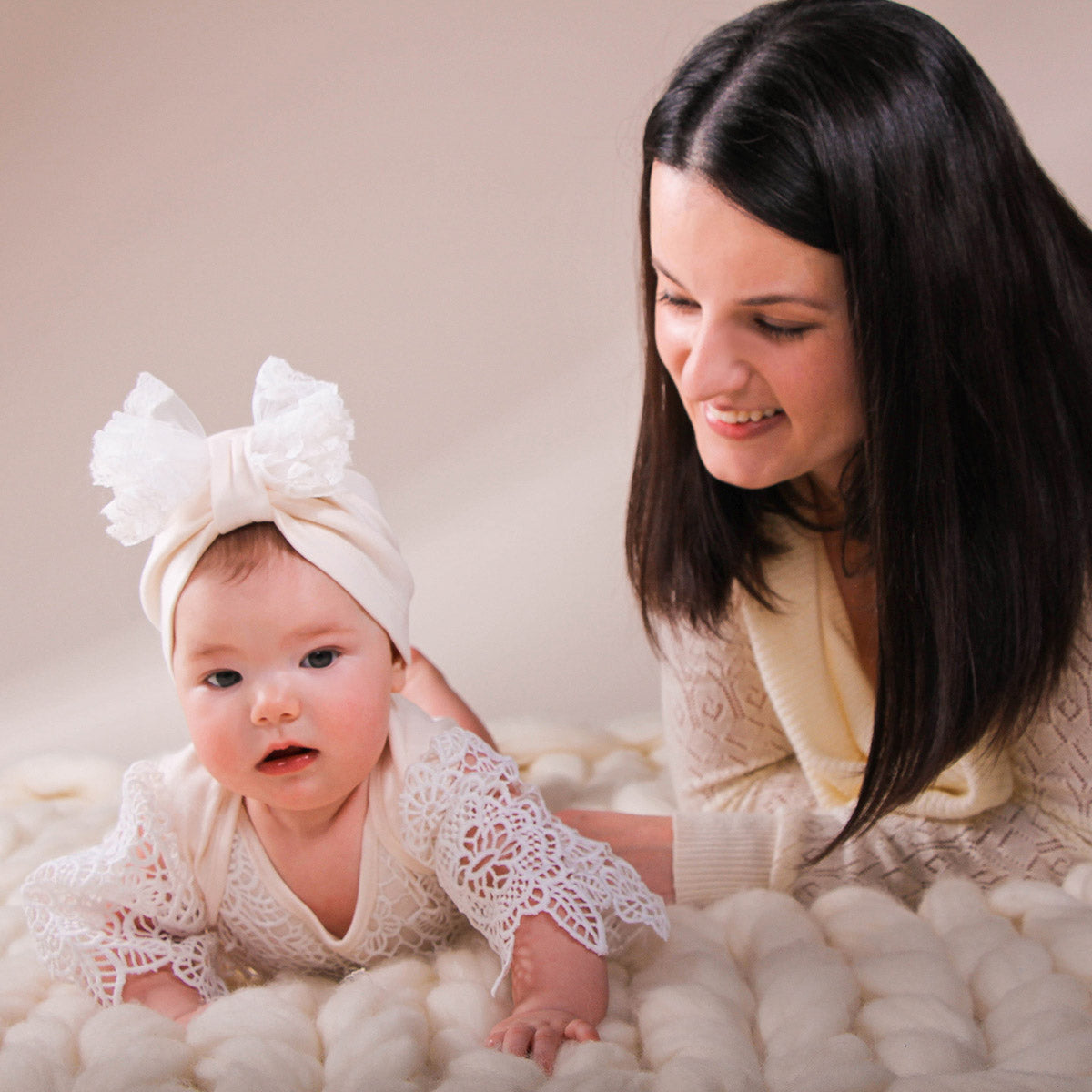 Woman and baby in white lace outfits on a soft surface