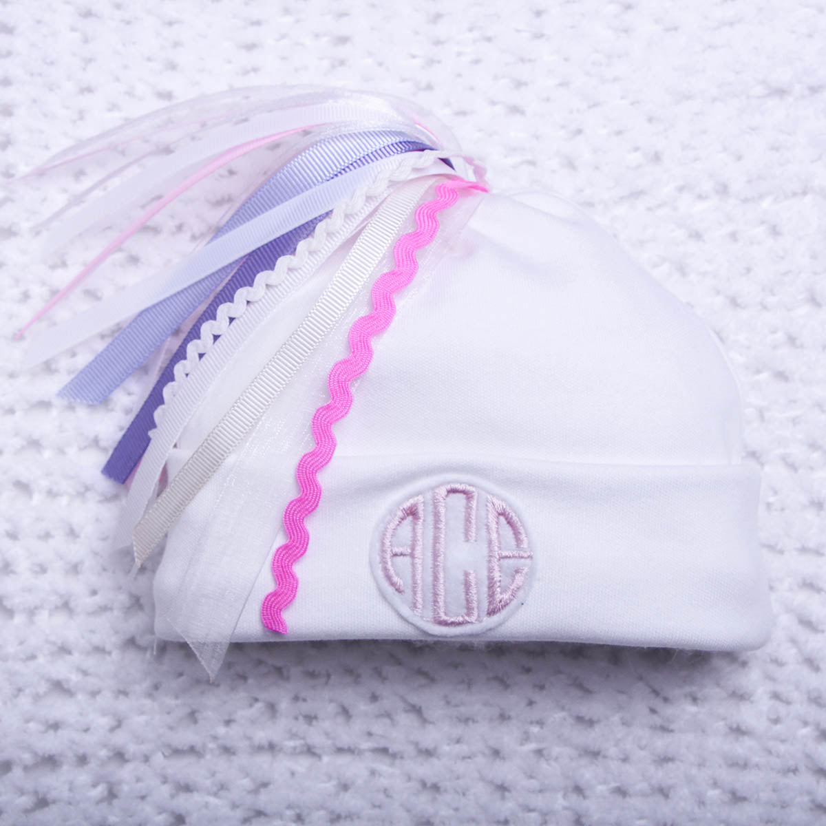 White pouch with pink and blue ribbons on a textured white background