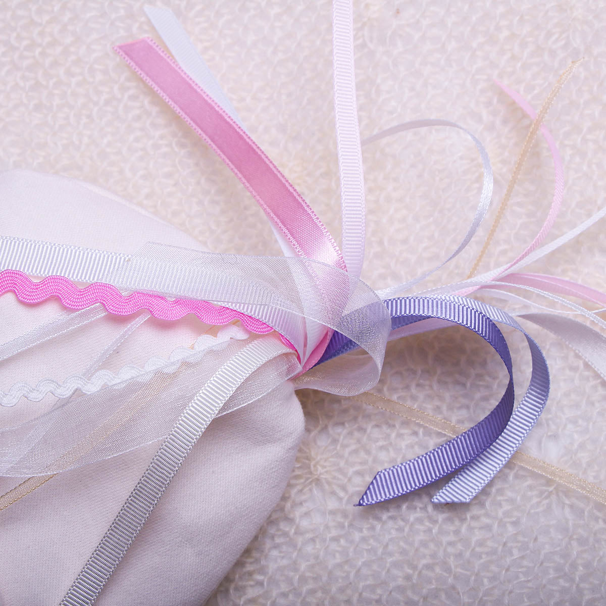 Close-up of ribbons with pink, white, and purple colors on a textured surface.