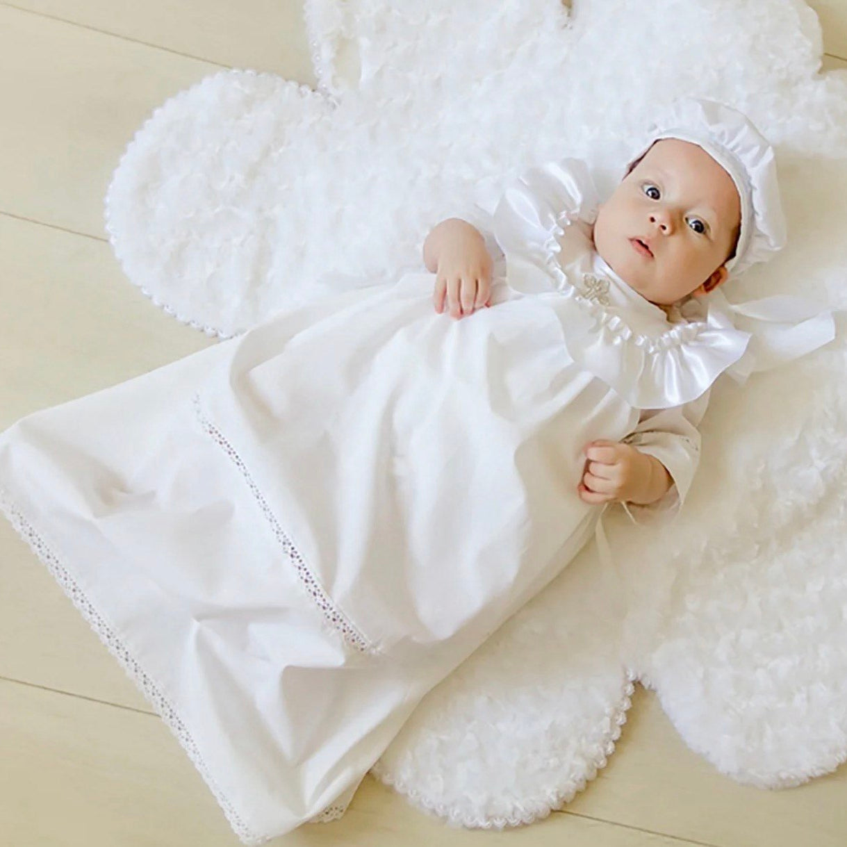 Baby in a white baptism outfit lying on a textured white blanket