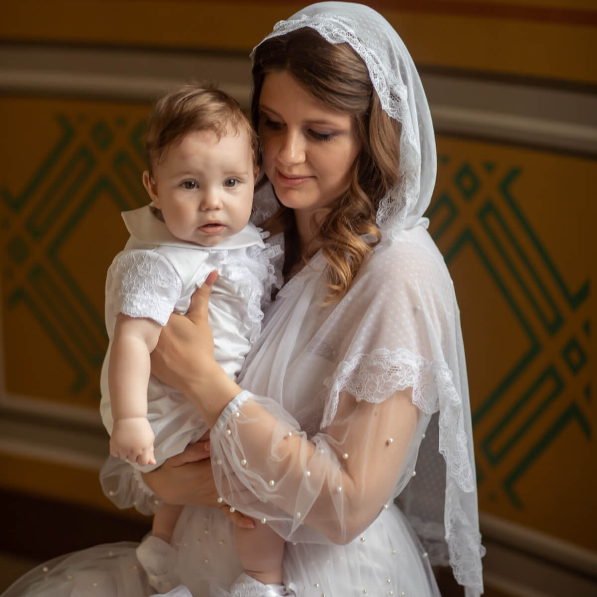 Woman in a Catholic Church Mantilla holding a baby with a decorative background