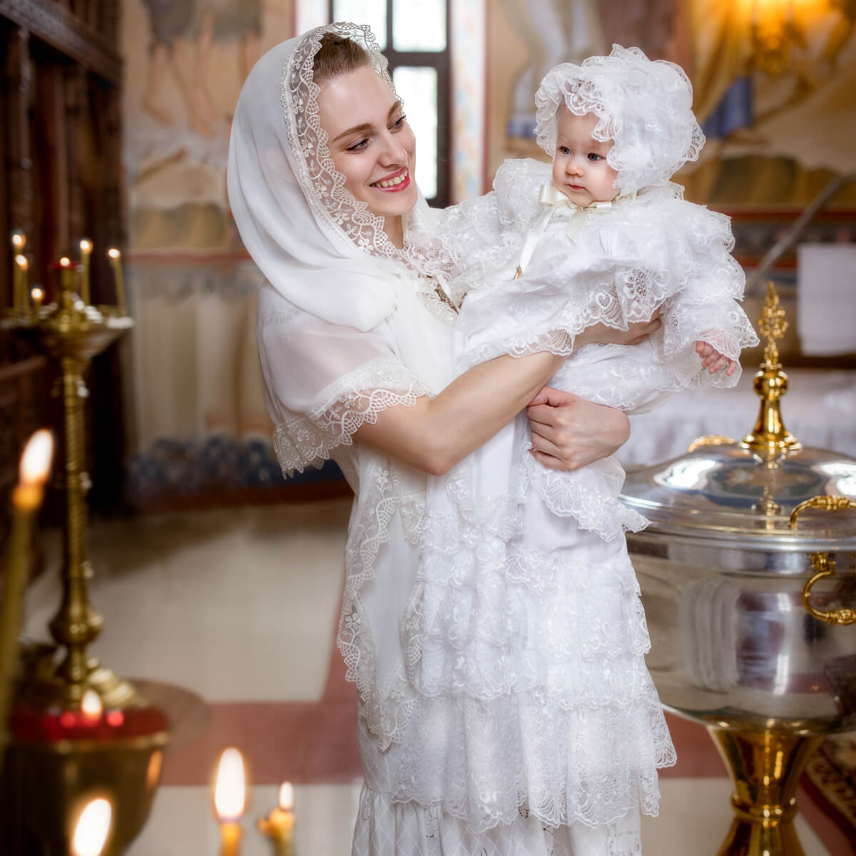 Woman in a christening gown holding a child in a church setting
