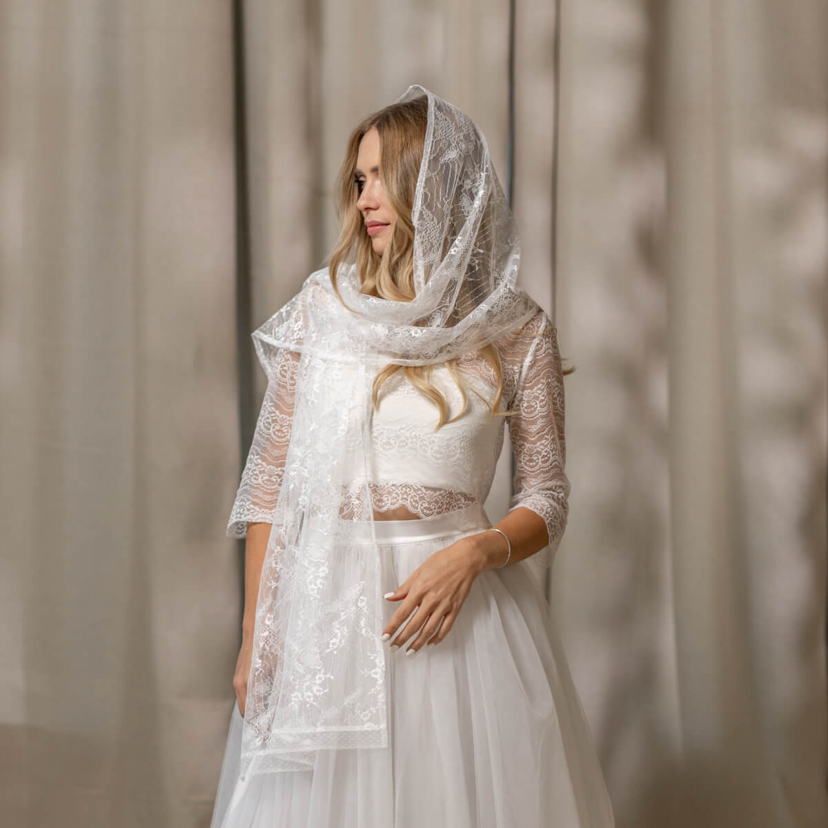 Woman wearing a lace wedding dress with a Lace Chapel Veil against a neutral background