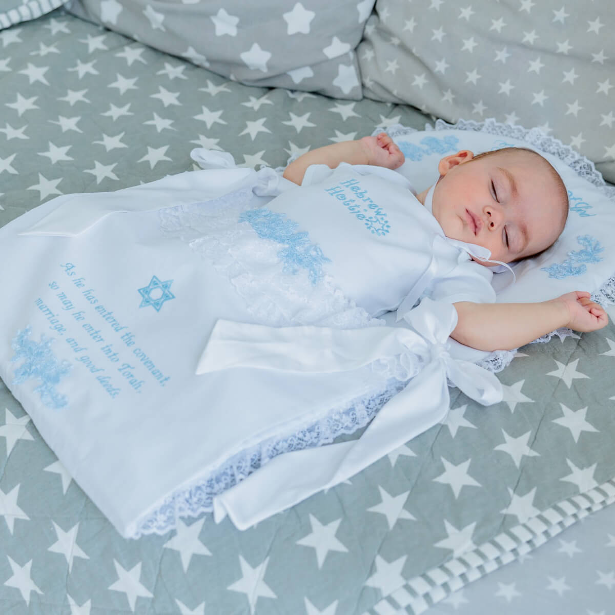 Baby wrapped in a white blanket with blue text on a star-patterned bed