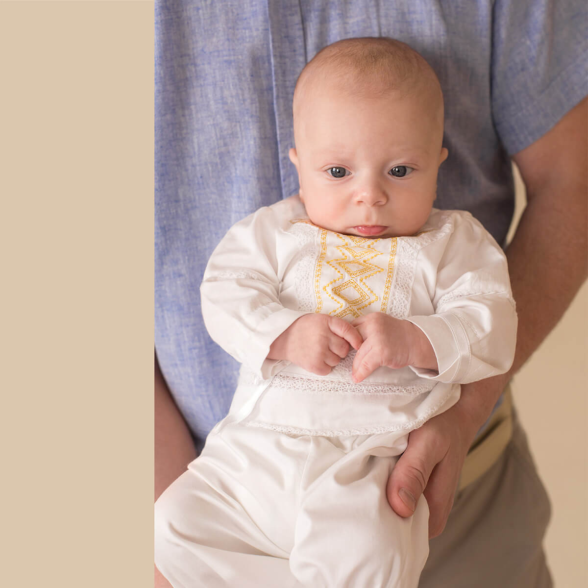 Baby wearing a Baby Boy Baptism Suit with intricate patterns, held by an adult.