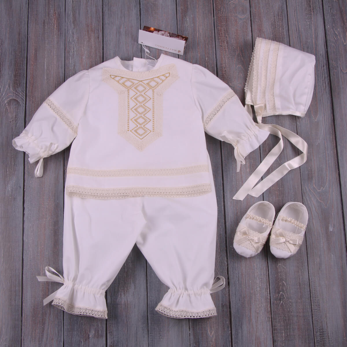 Baby Boy Baptism Suit with embroidered details, including a romper, shoes, and bonnet, on a wooden surface.
