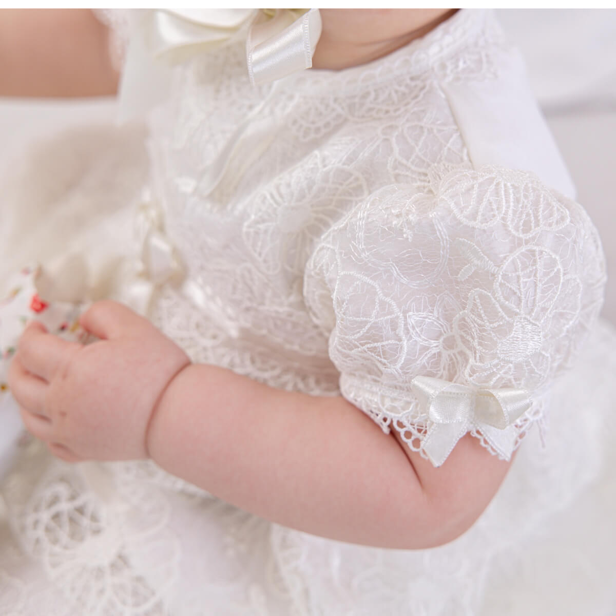 Close-up of a baby's arm wearing a Lace Baptism Dress with a bow.