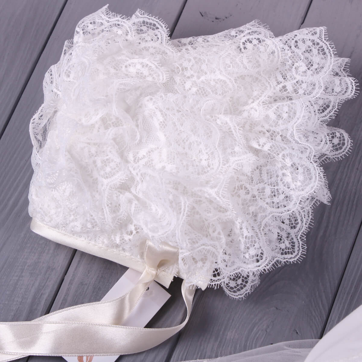 White Lace Baptism Bonnet with satin ribbon on a wooden surface