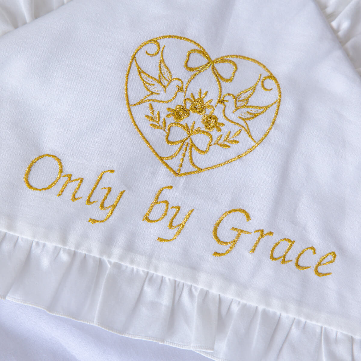 White fabric with gold embroidery of a heart, flowers, and 'Only by Grace' text.
