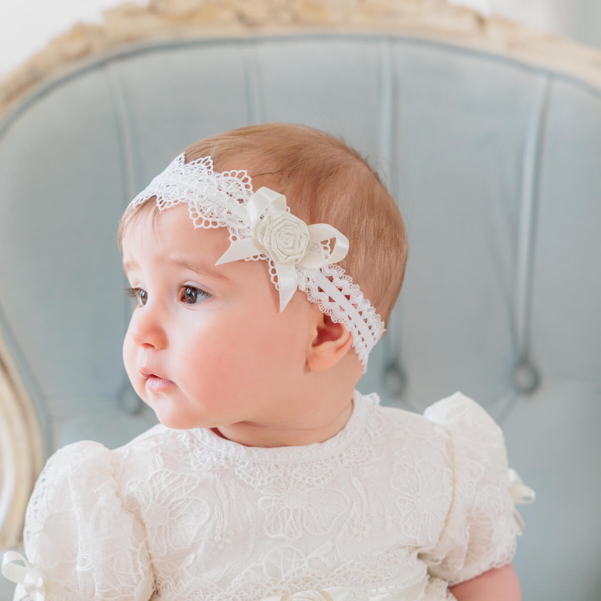 Girl wearing baby headband with a flower, sitting on a light blue chair.