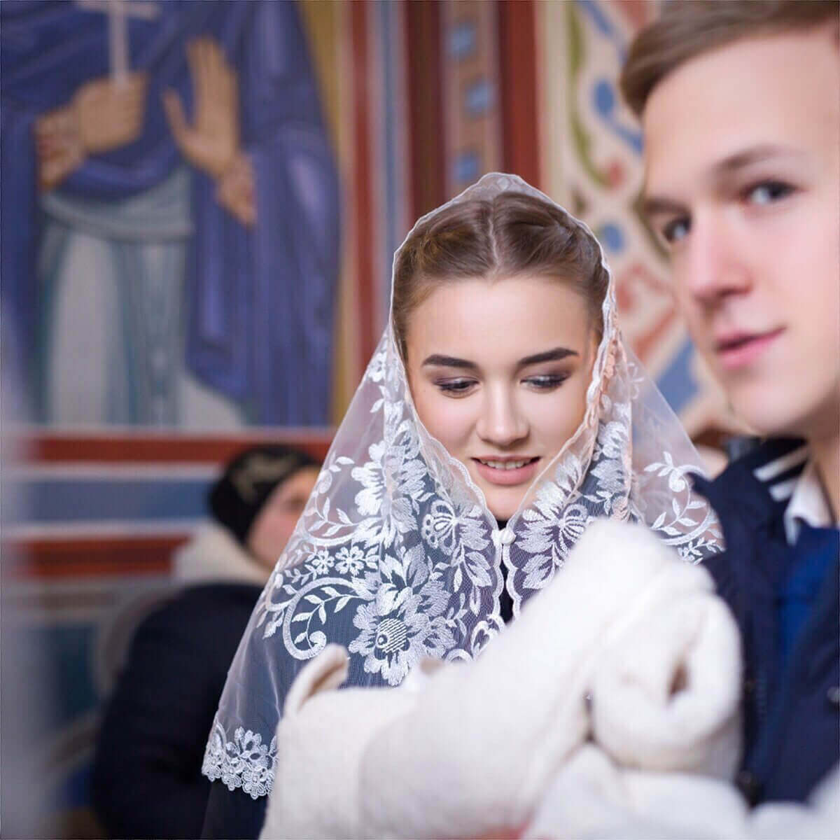 Woman wearing a Catholic Church Mantilla with lace details, holding a white rabbit, in front of a colorful mural.