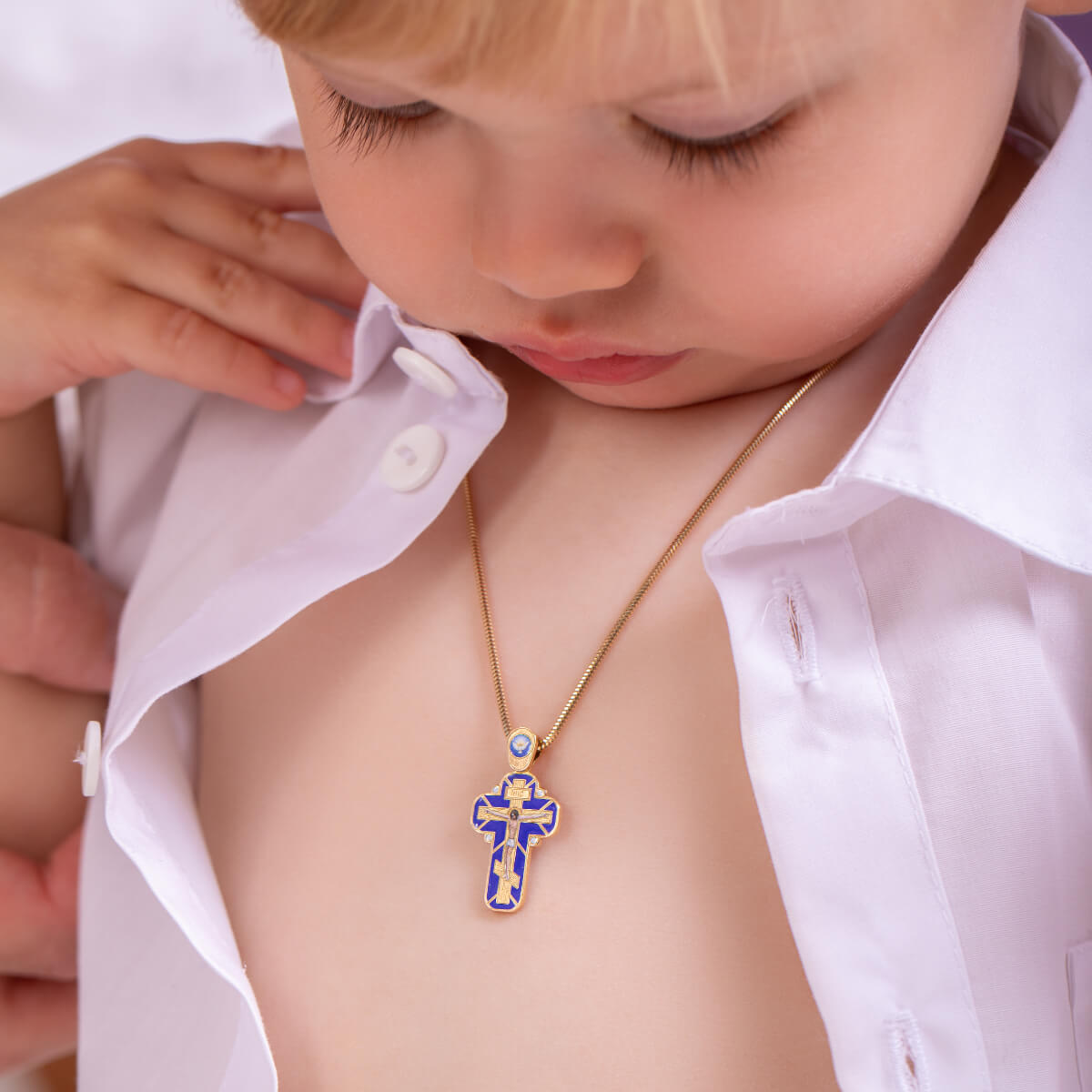 Child wearing a white shirt with a gold necklace featuring a SAVIOR Baptism Cross – Handcrafted Gold Enamel Crucifix