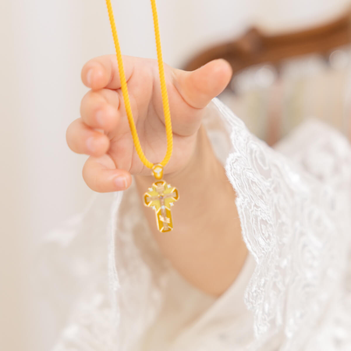 Hand holding a yellow necklace with a cross pendant against a blurred background