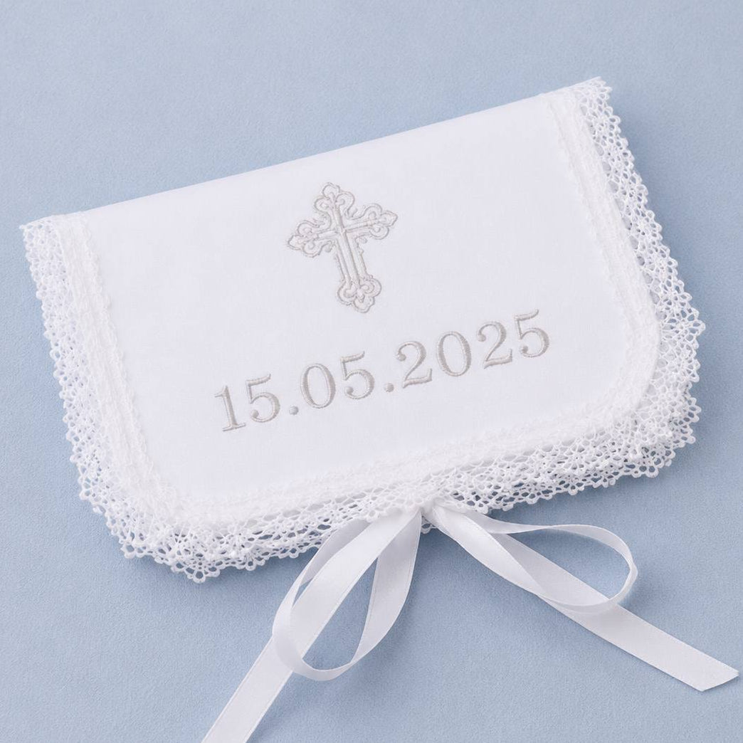A white embroidered baby baptism first curl keepsake with lace trim, featuring a silver cross and the personalized date '15.05.