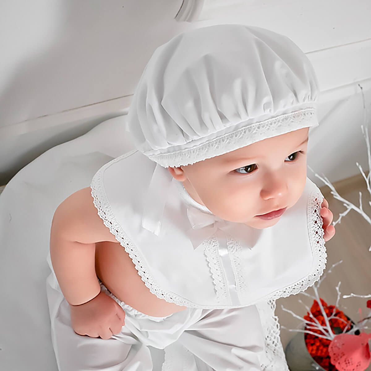 Baby wearing a white outfit with Boy Christening Hat on a light background