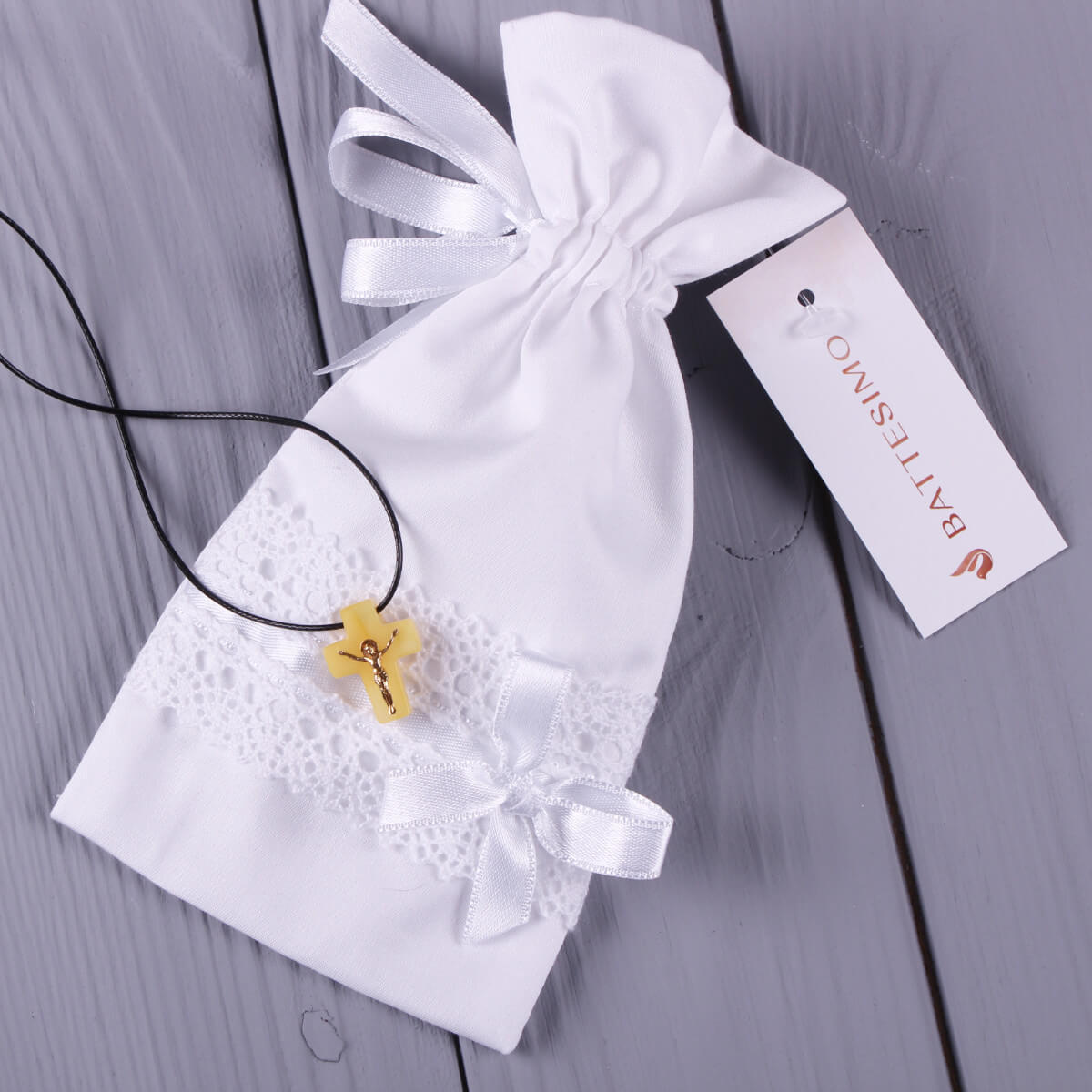 Baptism Keepsake Pouch for Cross in a white drawstring bag on a wooden surface