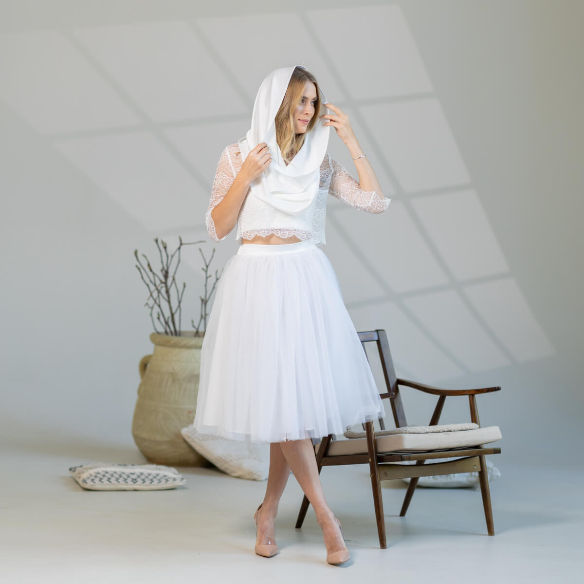 Woman in a white bridal outfit with a Chapel Mantilla in a minimalistic room.