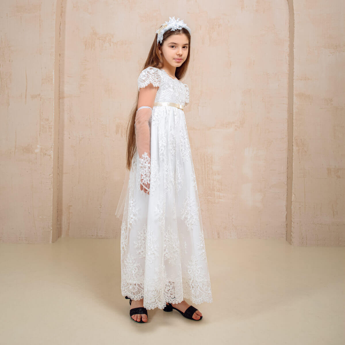 Young girl in a white communion lace dress standing against a plain background