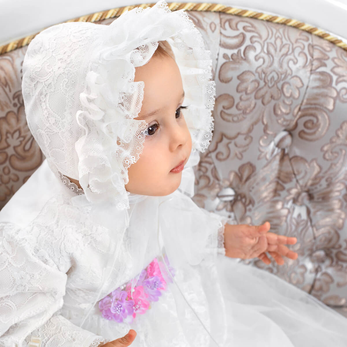 Baby in a lace baptism bonnet with a decorative background