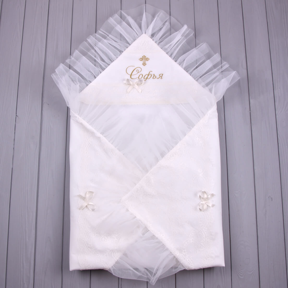 White christening blanket with tulle and embroidered name on a wooden surface