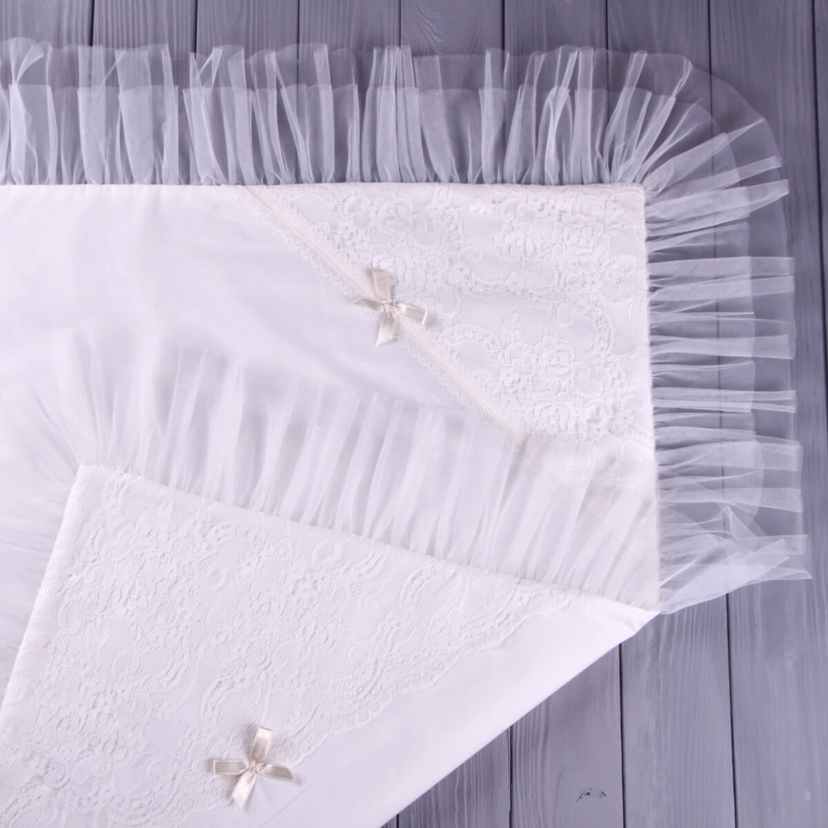 White lace christening blanket with tulle border on a wooden surface