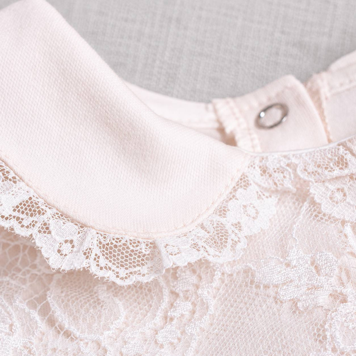 Close-up of a liliana lace romper. featuring a wide fabric collar with white lace trim and a small silver metal snap button.