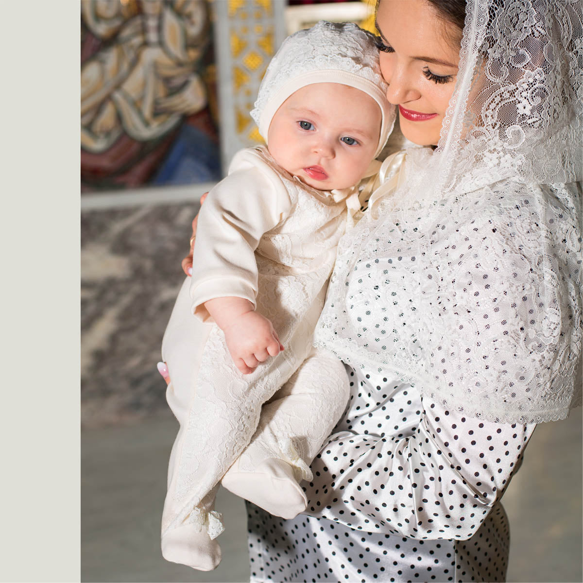 Woman holding a baby dressed in Caped Lace Veil with a patterned background