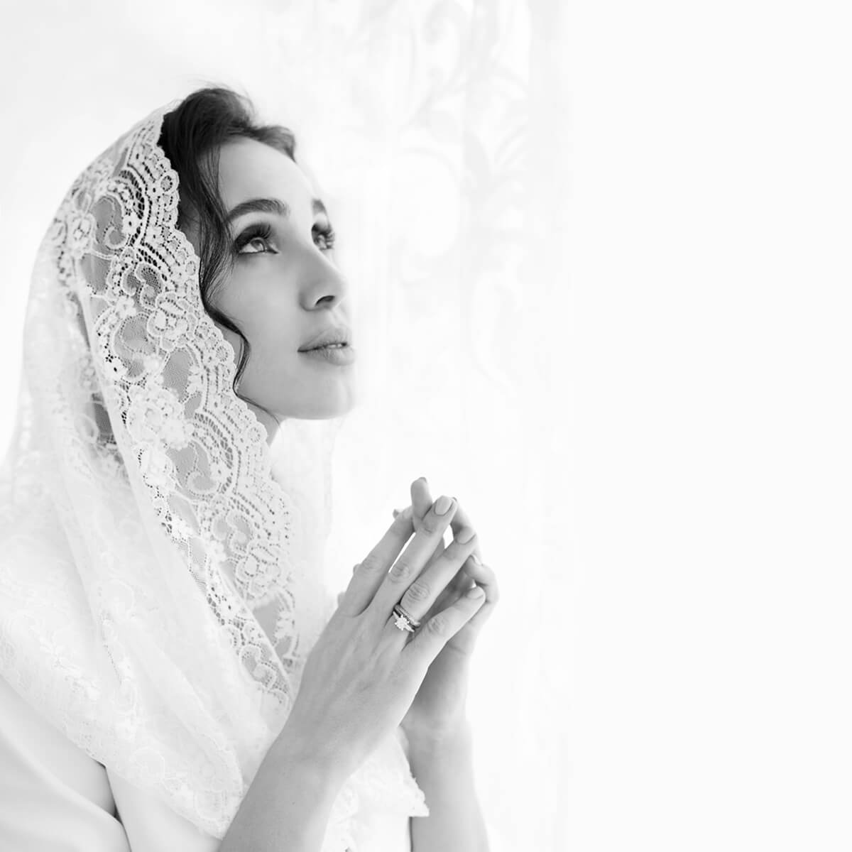Black and white photo of a woman wearing a Catholic Infinity Veil with hands clasped together.