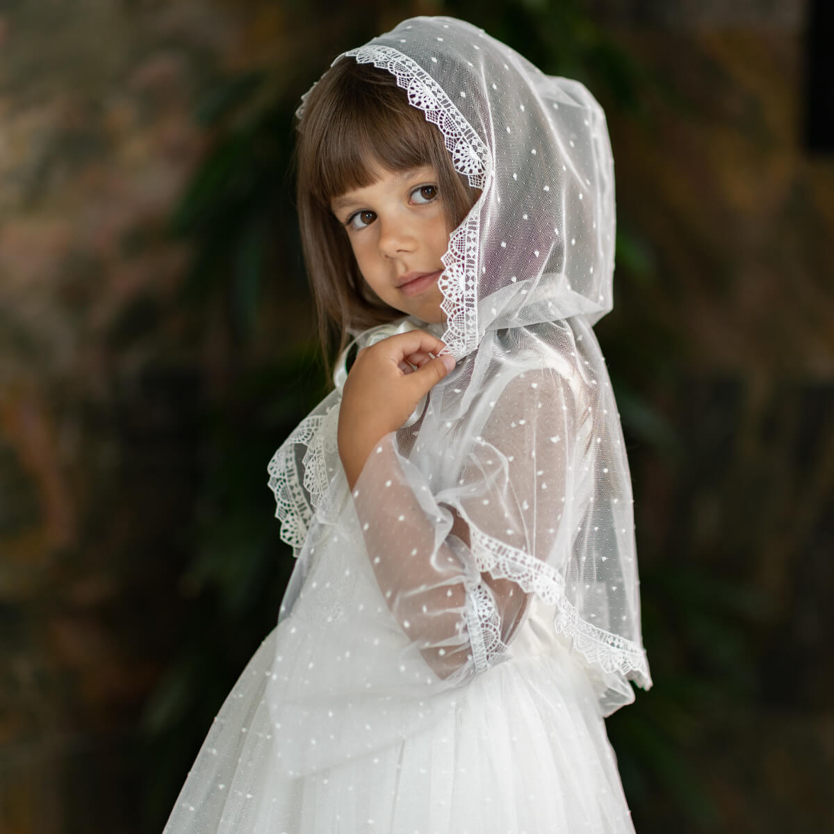 Young girl wearing a white lace veil against a blurred natural background