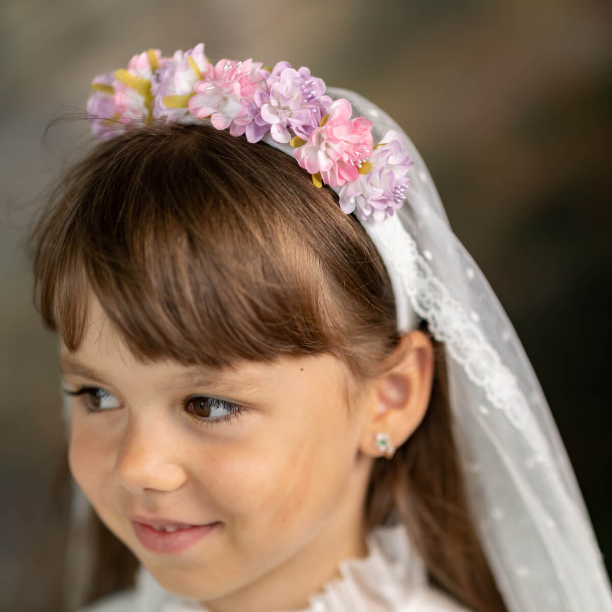 Young girl wearing a floral headband and veil, looking to the side.