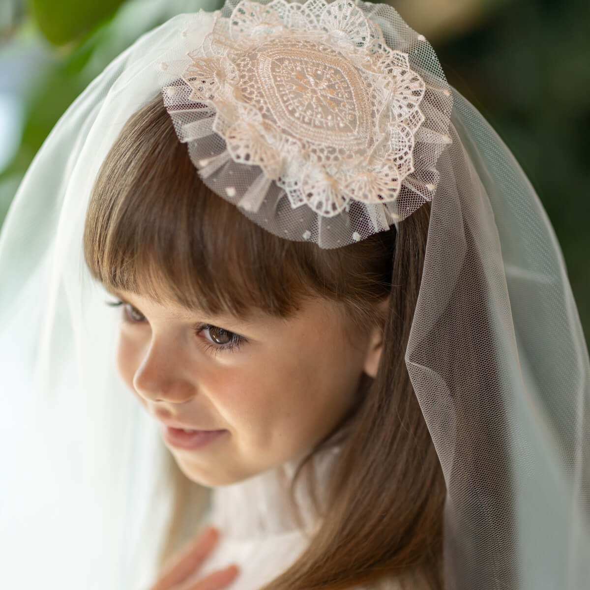 Young girl wearing a First Communion Veil with lace details against a blurred natural background