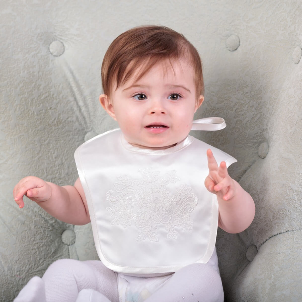 Baby wearing a Newborn Bib with Lace sitting on a gray cushion