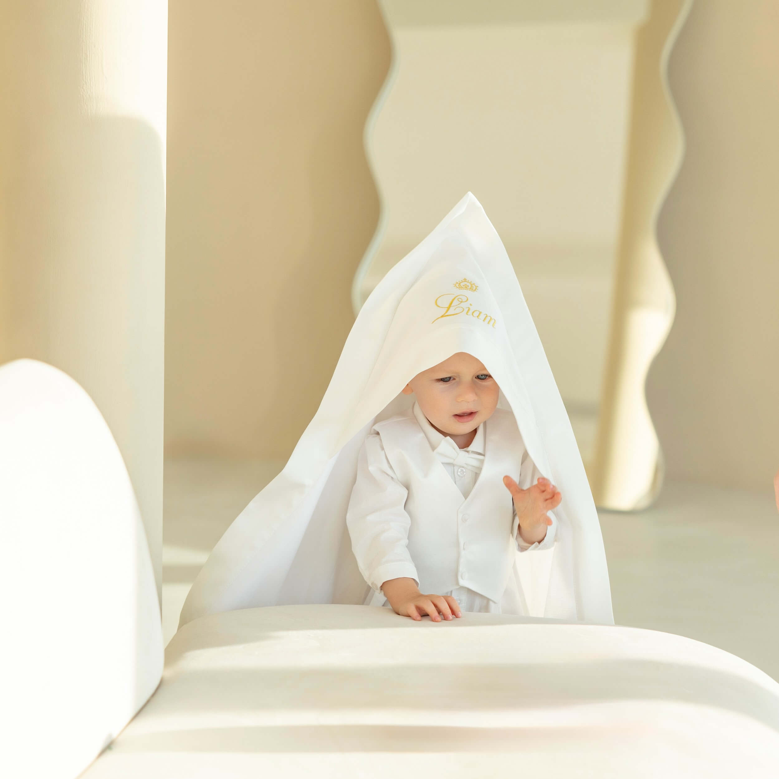 Baby in ivory baptism blanket peeking out from under a white canopy with a brand logo.