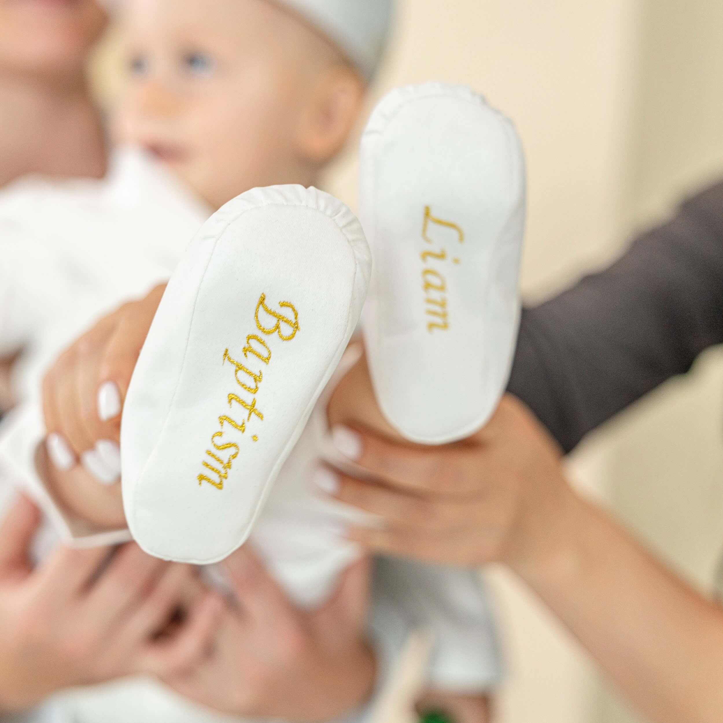 Christening Booties with 'Baptism' and 'Liam' embroidered on them, held by a person.