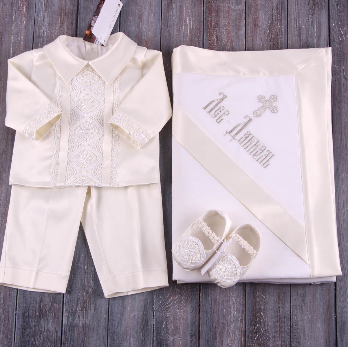 Baby outfit with shirt, pants, Christening Booties, and blanket on a wooden surface