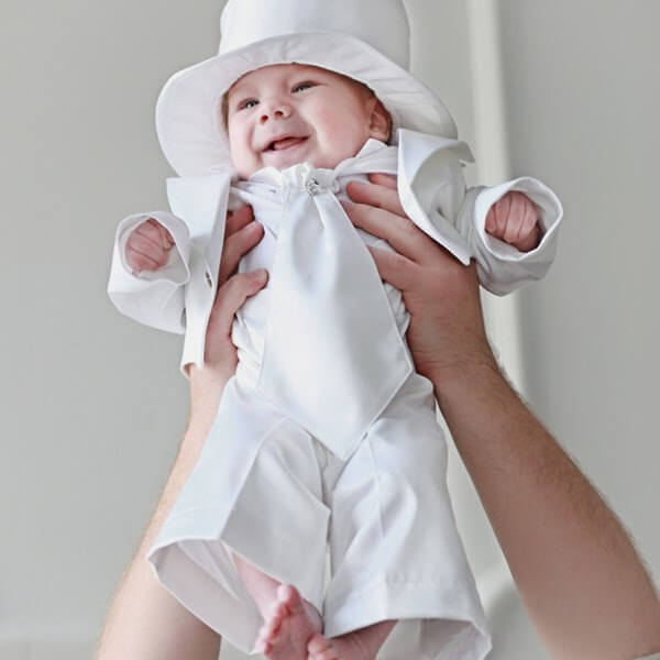 Baby in a white outfit and Boy Christening Hat being held against a plain background