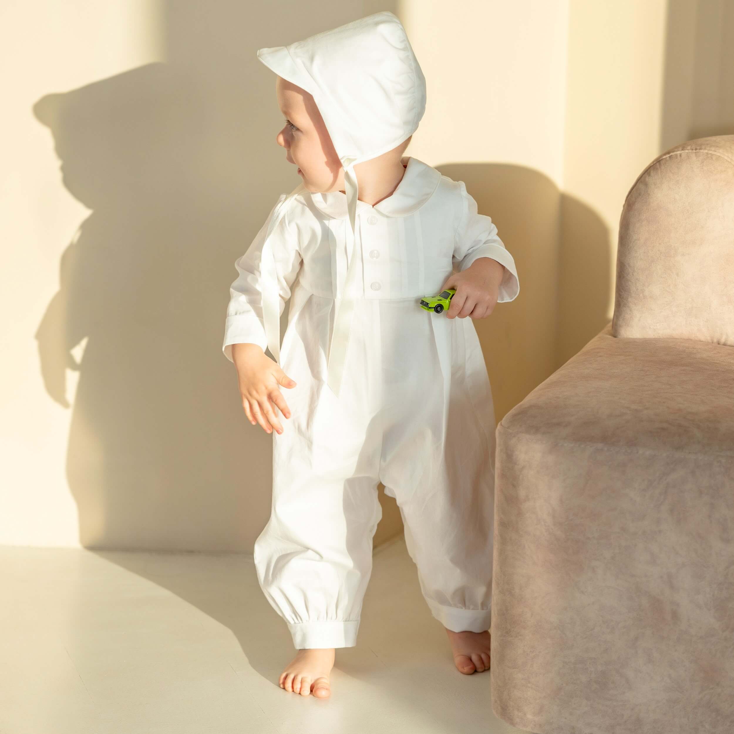 Baby in a Boy Christening Hat standing on a light-colored floor with a neutral background