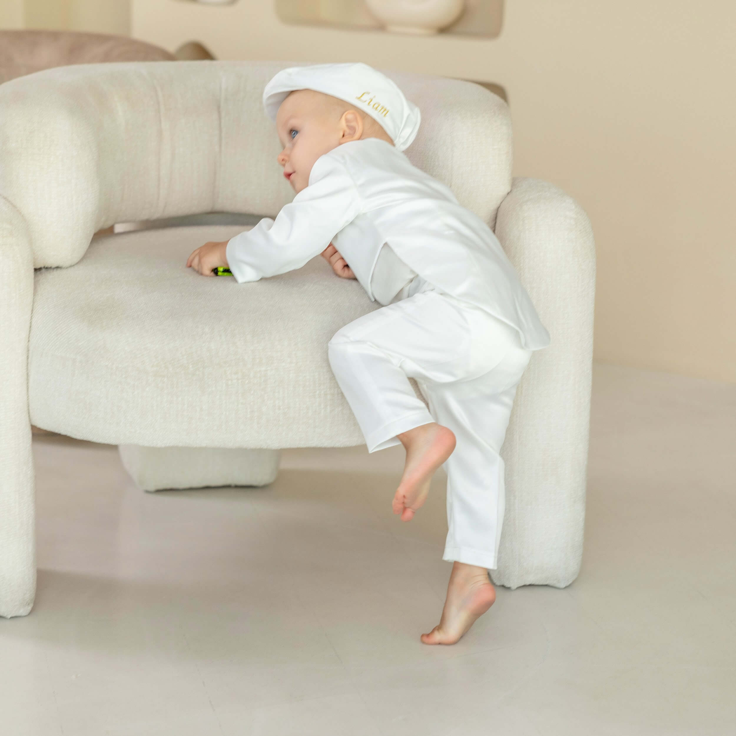 Baby in a Baptism Suit for Baby Boys sitting on a beige armchair.