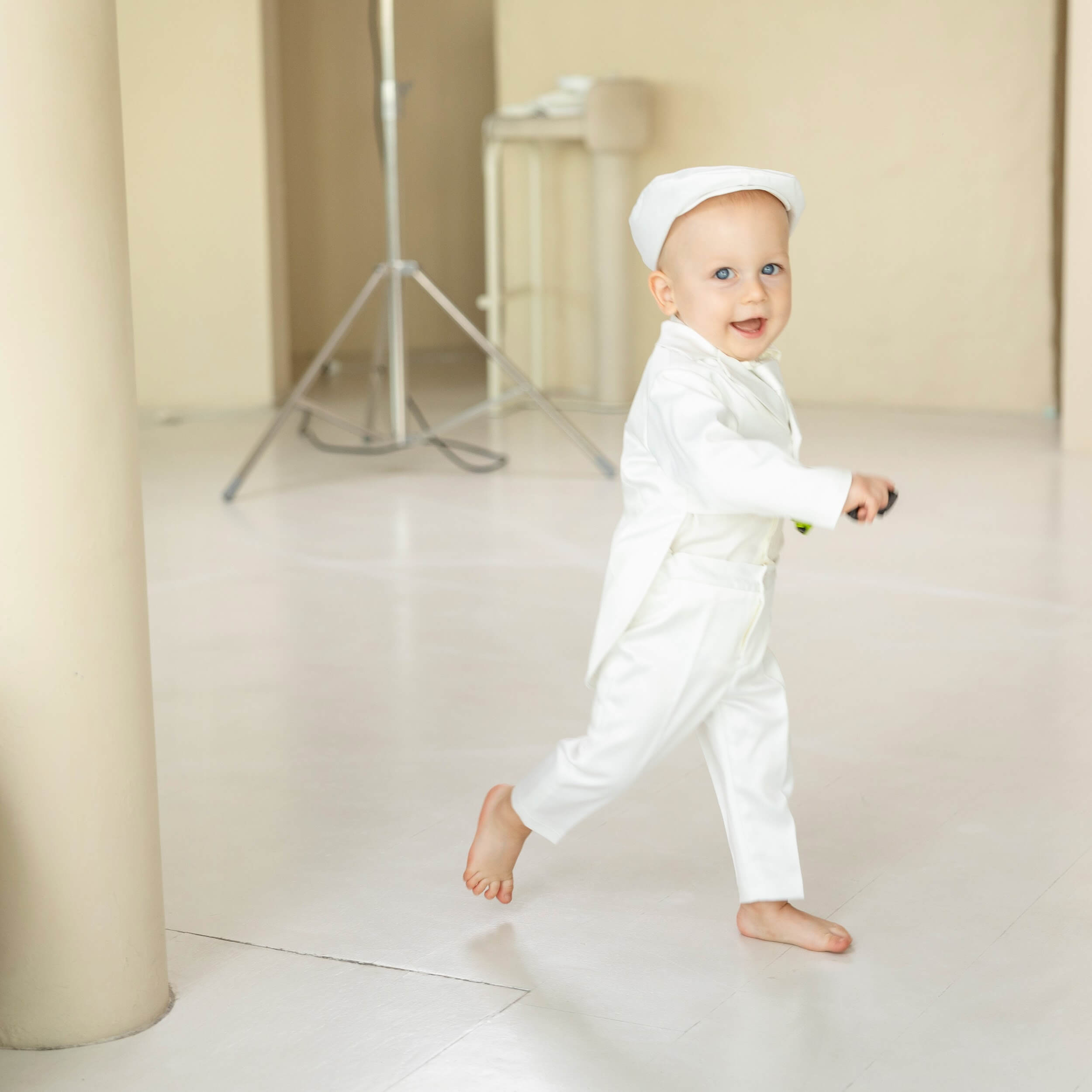 Baby in a Baptism Suit for Baby Boys standing in a minimalistic room with neutral colors.