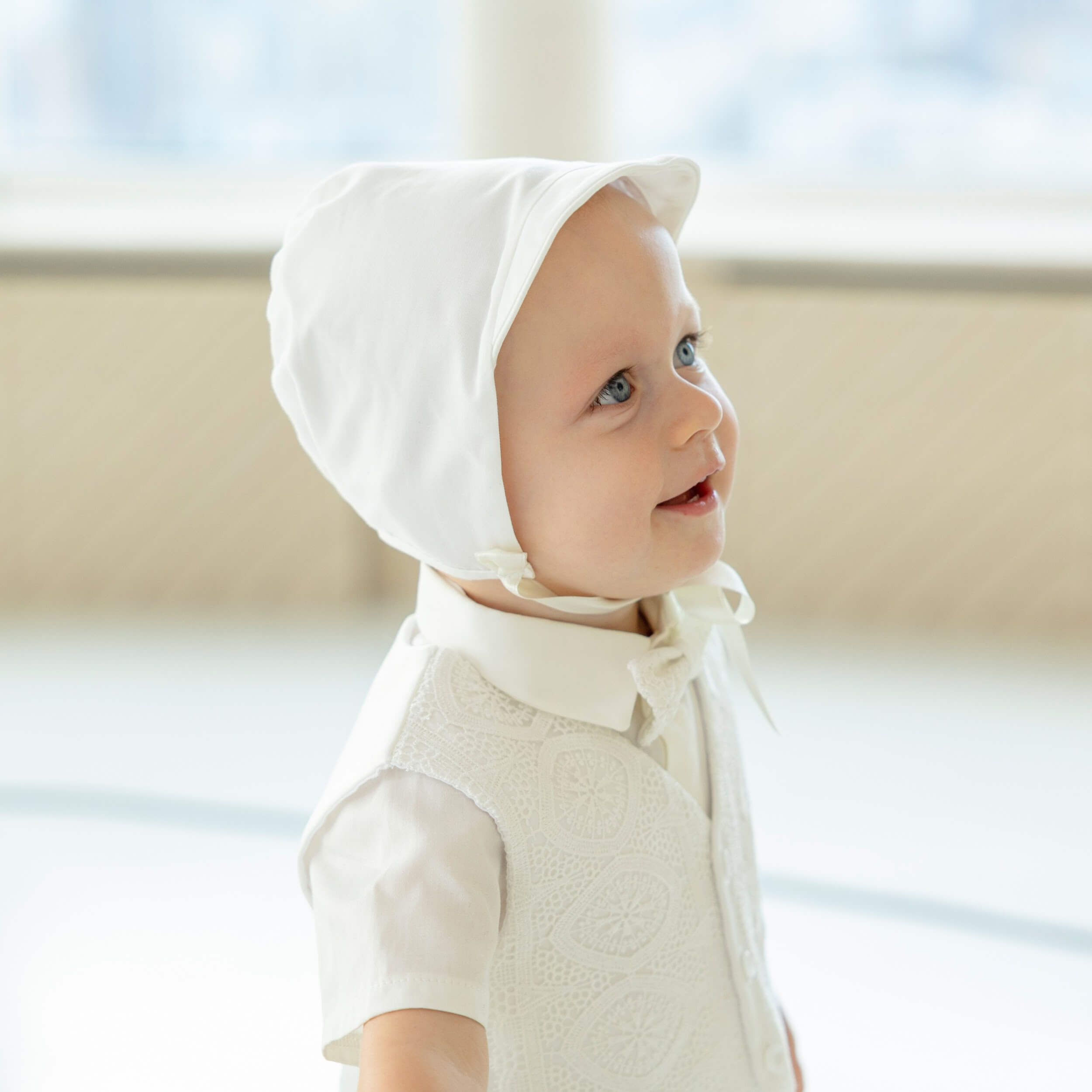 Baby wearing a Boy Christening Hat in a softly blurred indoor setting