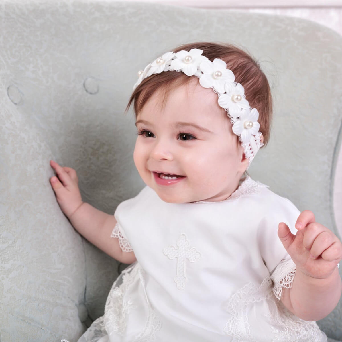 Baby wearing a Girl Christening Gown with pearls on a neutral background