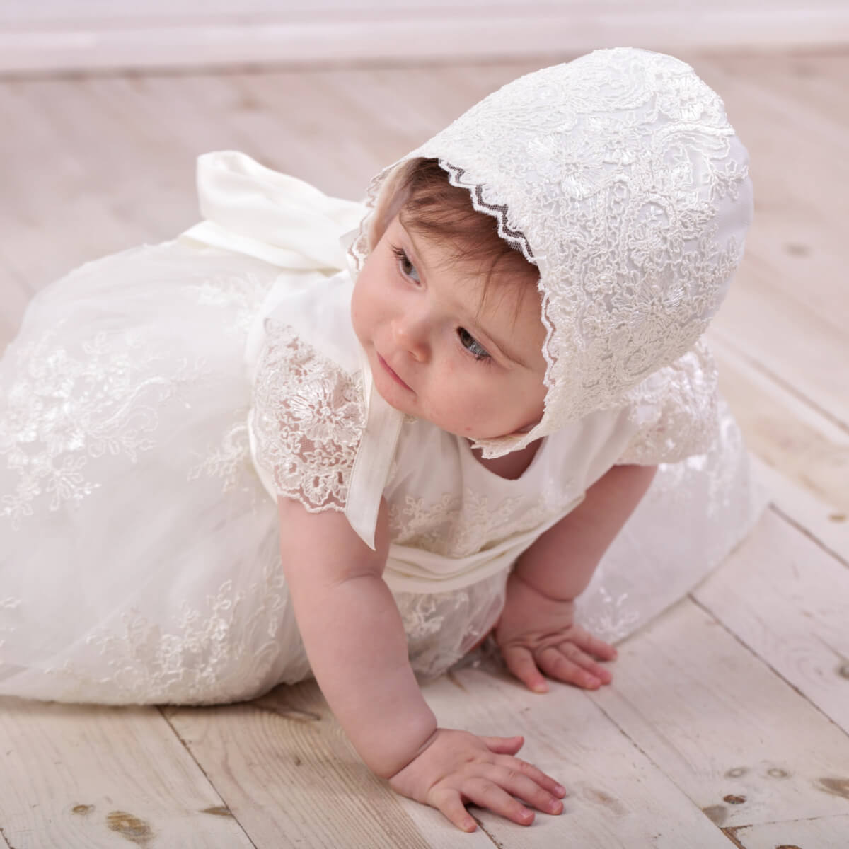 Baby in a Elegant Christening Dress and bonnet on a wooden floor
