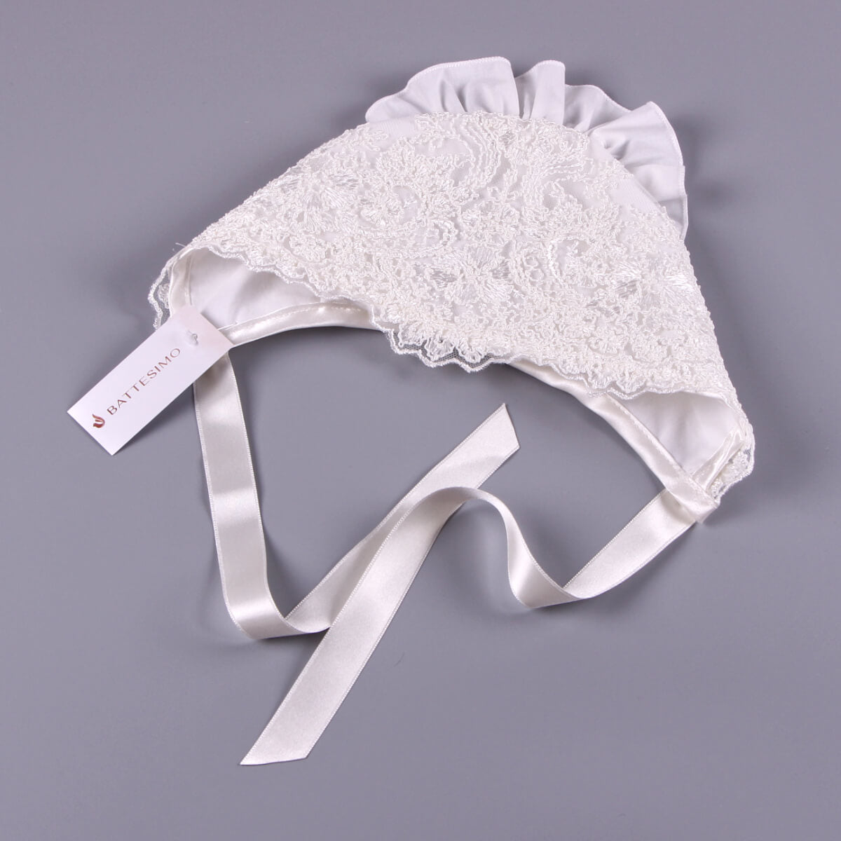 White Lace Baptism Bonnet with satin ribbon on a gray background