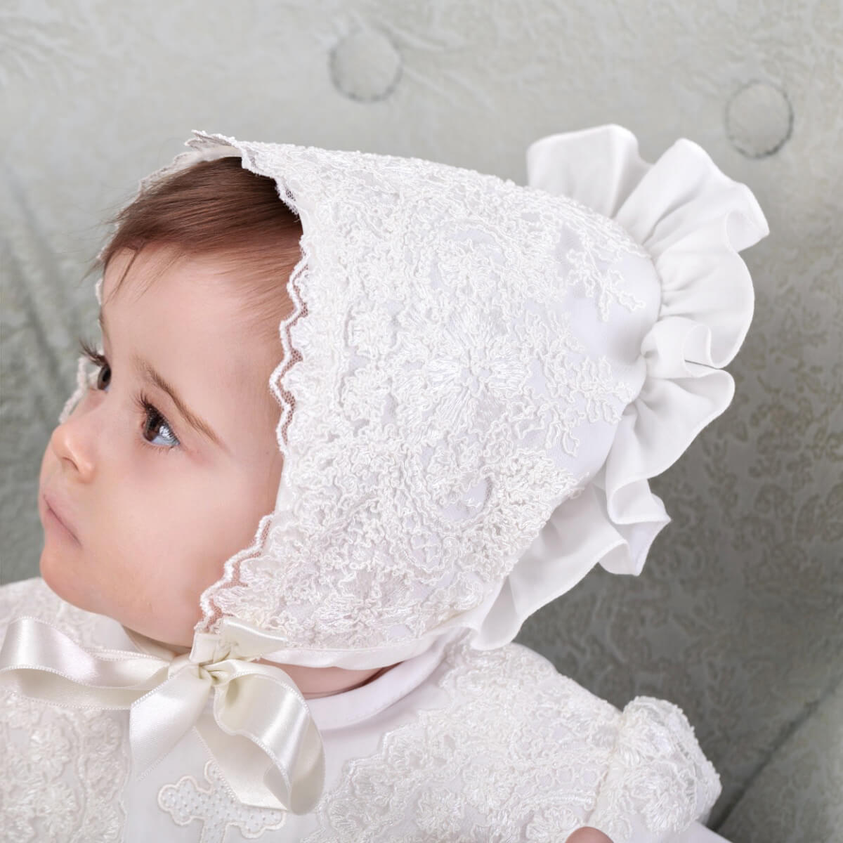 Baby wearing a Lace Baptism Bonnet with a bow against a neutral background