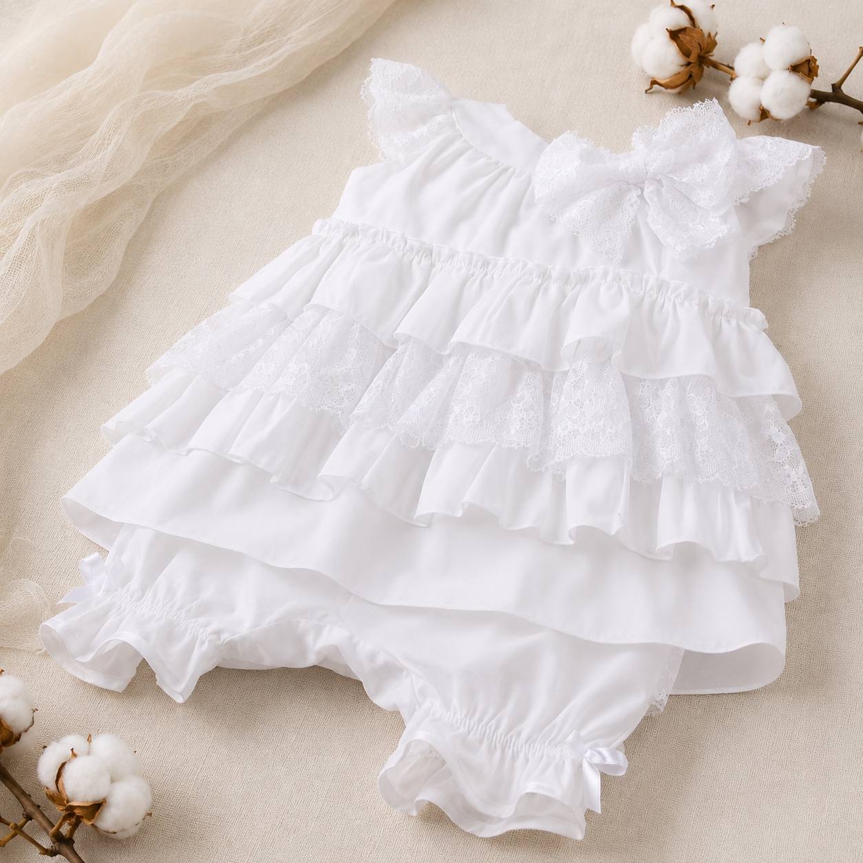 White ruffled dress with bloomers on a beige background with cotton branches.