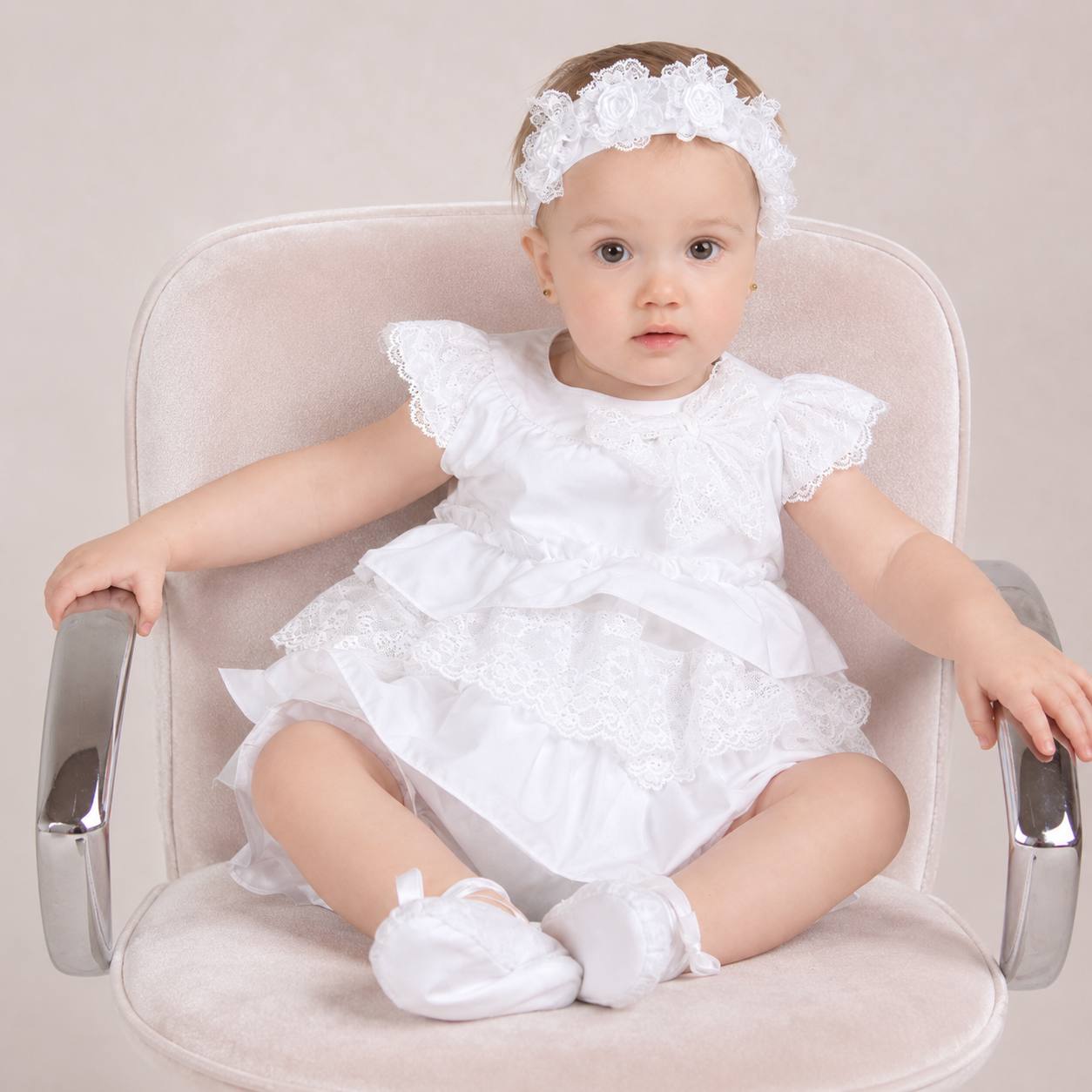 Baby in a white summer dress sitting on a chair with a neutral background